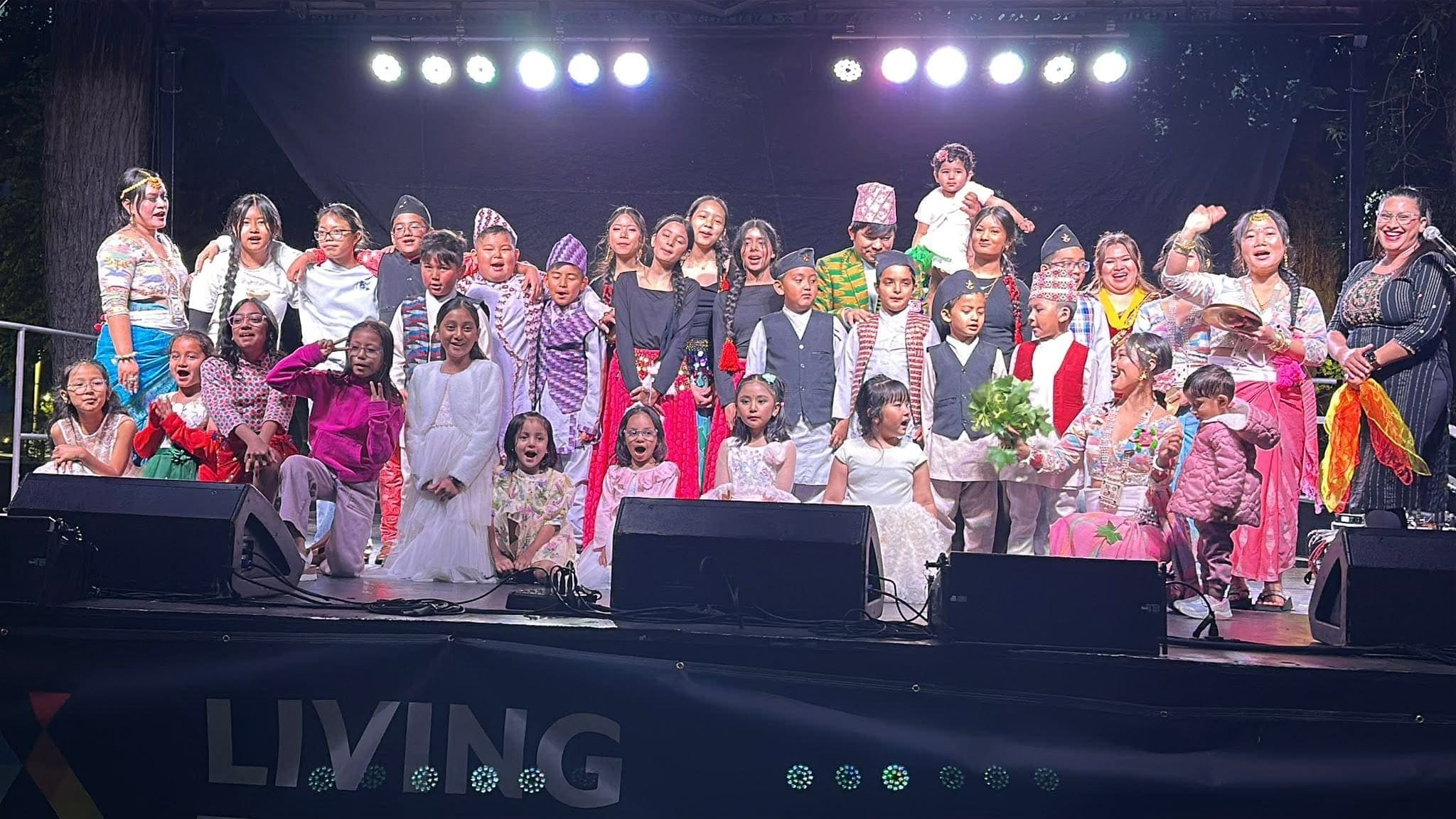 Children and adults in Nepali dress filling a festival stage at the end of a performance