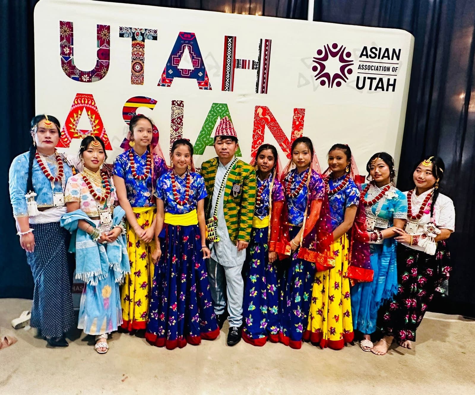The dance group in traditional Nepali dress in front of the Utah Asian Festival backdrop
