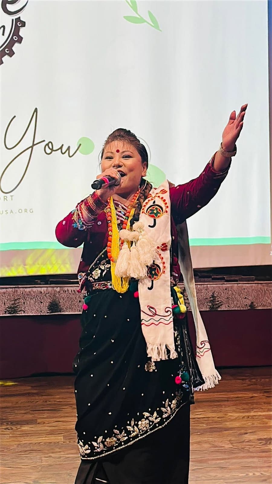 A singer in traditional dress performing with a microphone, one arm raised